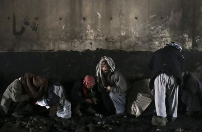 Afghan drug addicts cover their heads with scarves as they use drugs under a bridge inhabited by drug addicts in Kabul